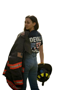 Woman wearing jeans and a firefighter T-shirt looks over her shoulder, holding a firefighter jacket and helmet, standing against a plain white background. Ready to make a difference? Join Devola Volunteer Fire Company—volunteer today!.